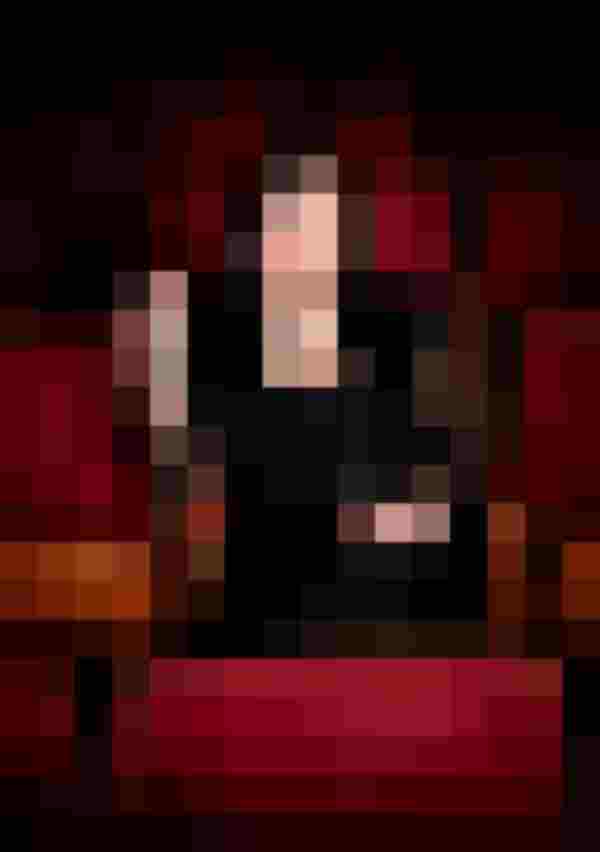 Frau in schwarzer Kleidung sitzt in rotem Theatersaal