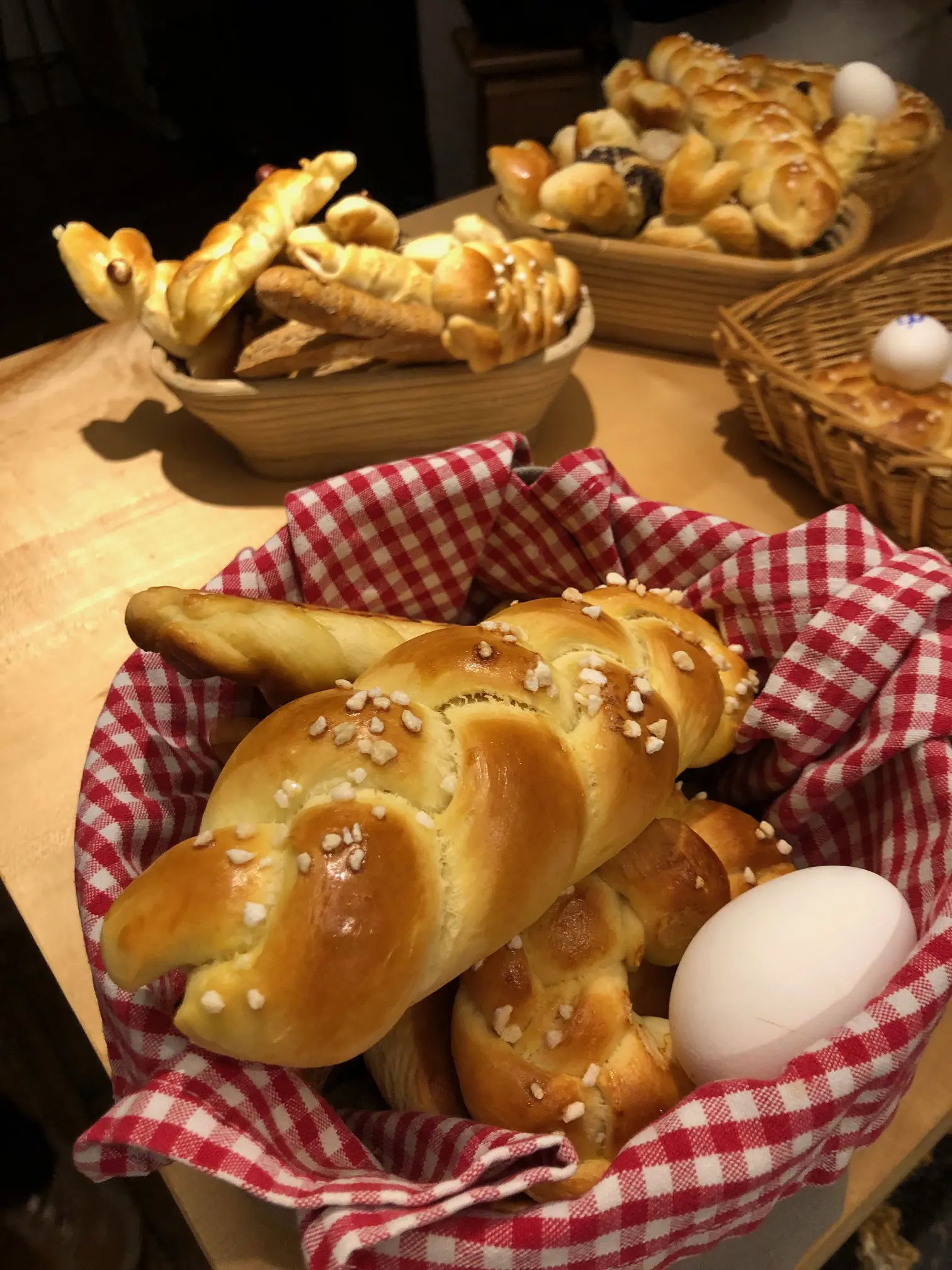 Frisches Bauerngebäck und ein Ei in einem Korb mit kariertem Tuch, rustikale Atmosphäre.