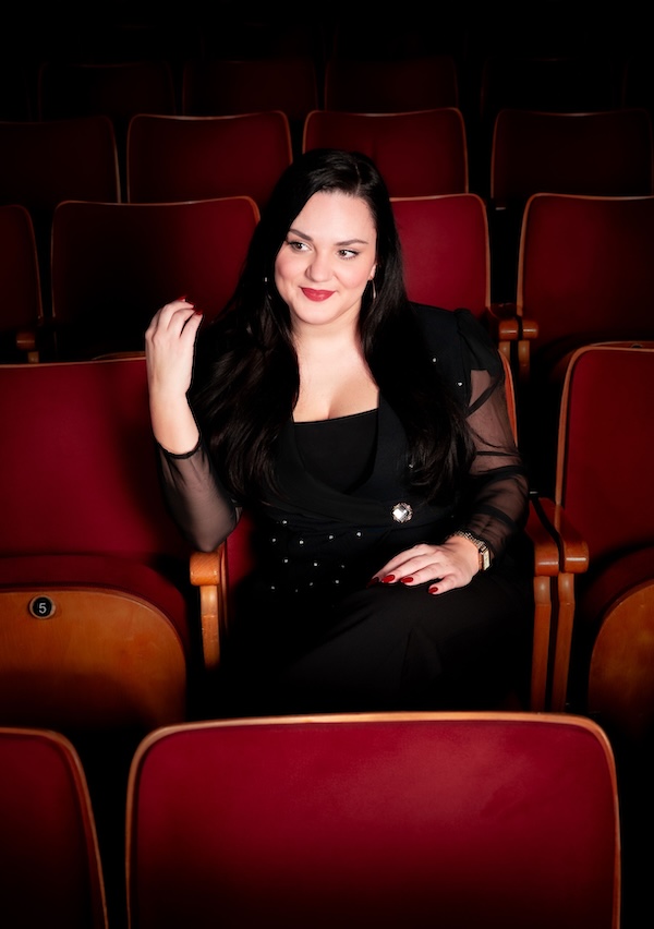 Frau in schwarzer Kleidung sitzt in rotem Theatersaal