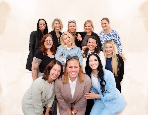 Gruppenporträt von elf lächelnden Frauen in drei Reihen vor hellem Hintergrund
