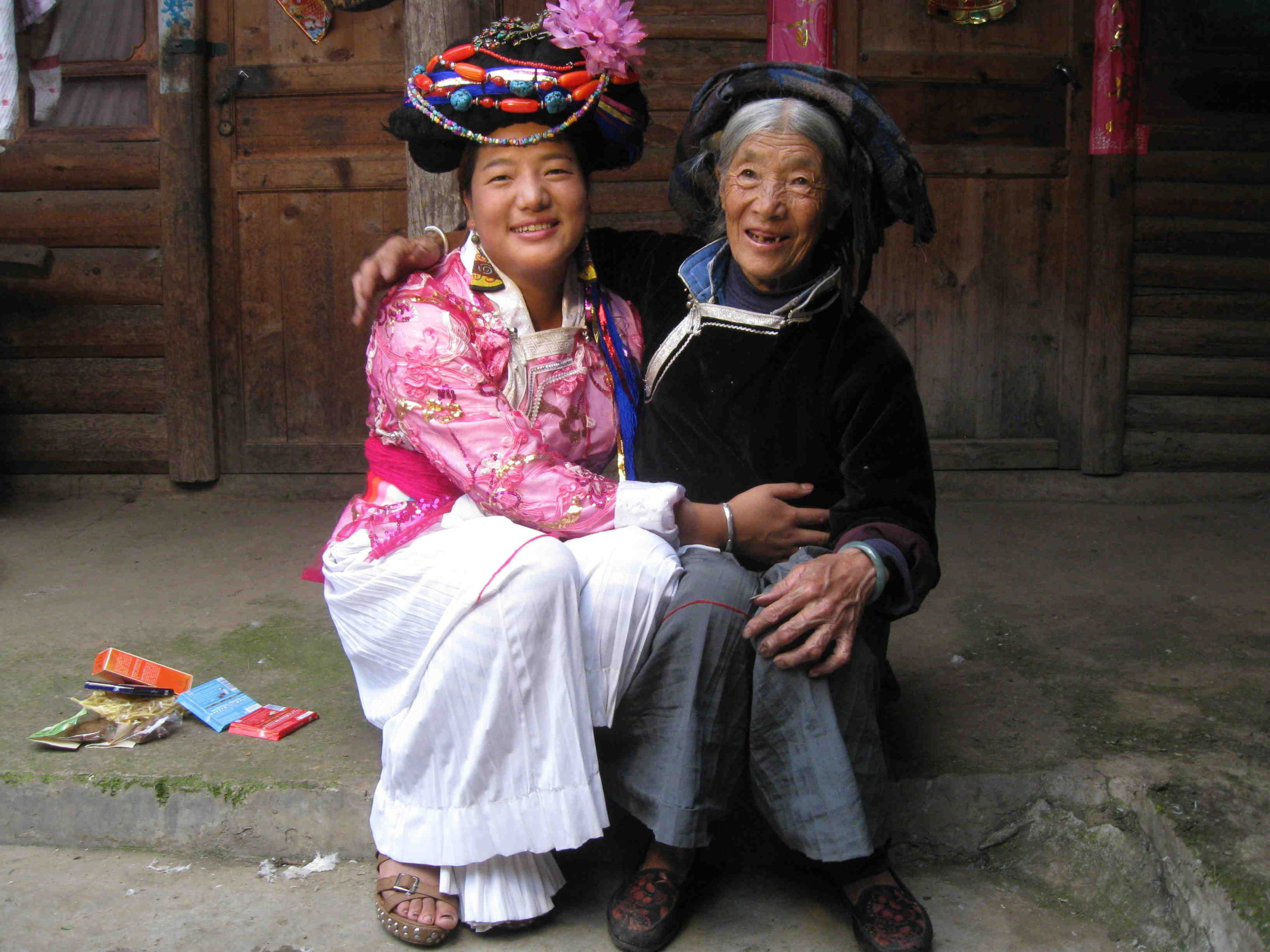 Zwei Frauen in traditioneller Kleidung sitzen lächelnd vor einer Holztür